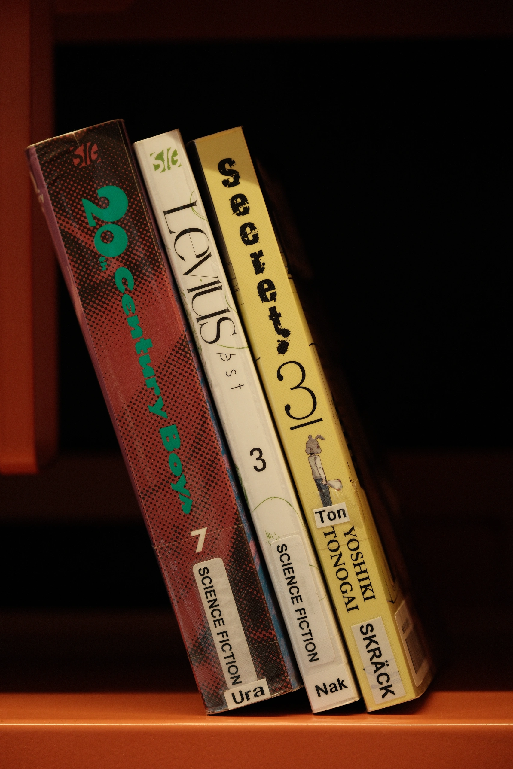 Three numbered science-fiction books leaning together on an orange shelf