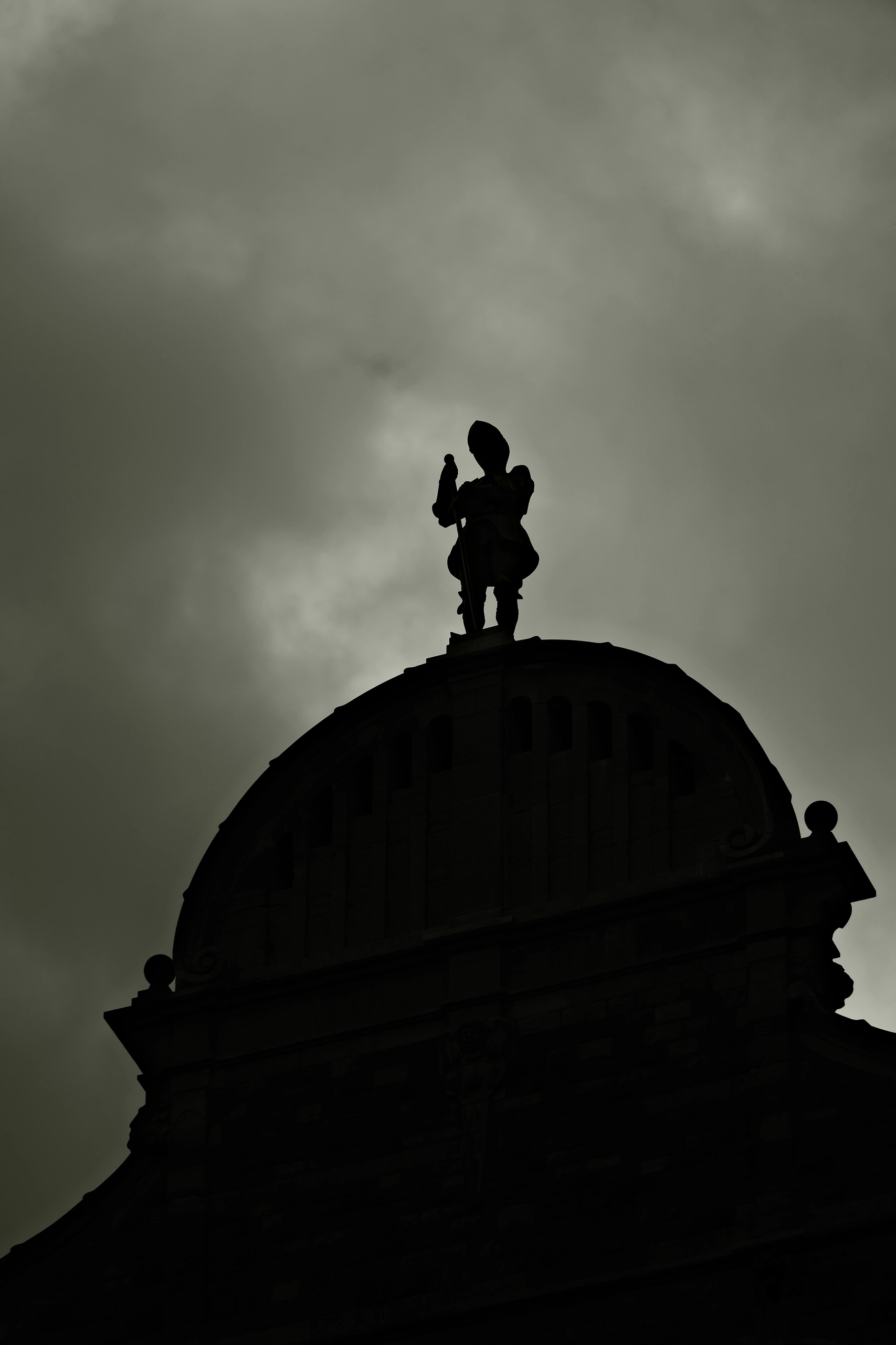 Silhouette of a rooftop sculpture and domed building against a cloudy sky