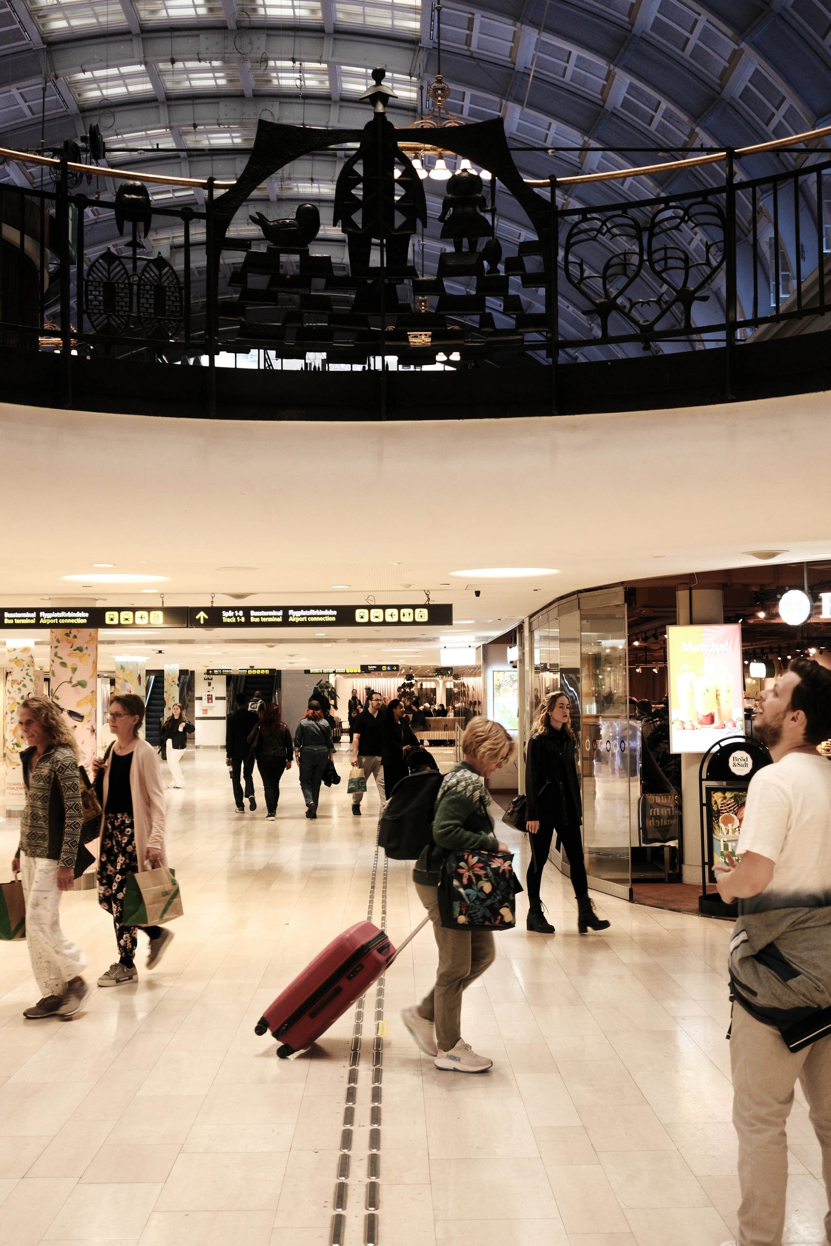 Travellers walking through a busy terminal below decorative metal figures