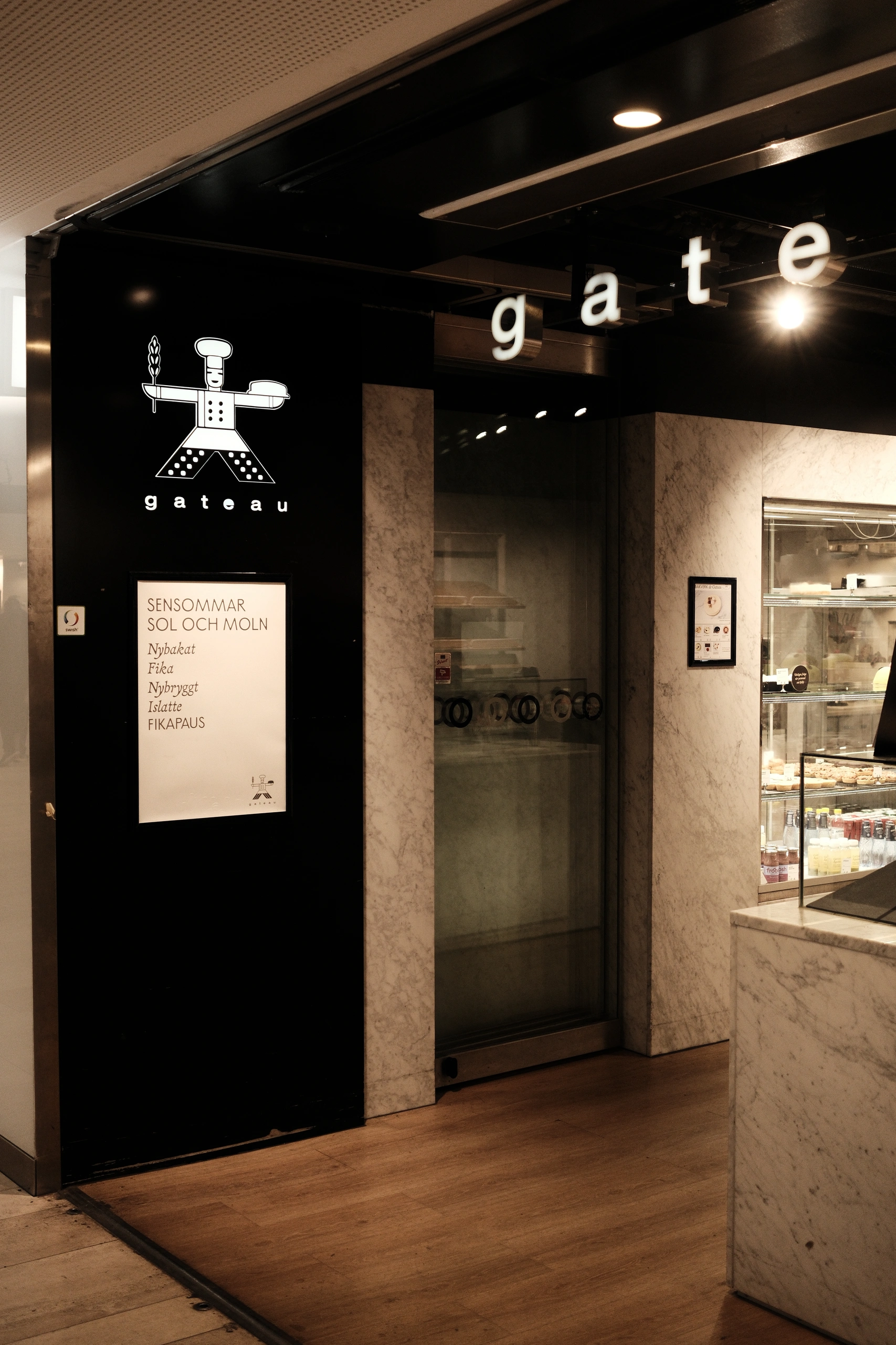 Black and marble bakery entrance with illuminated letters spelling gateau