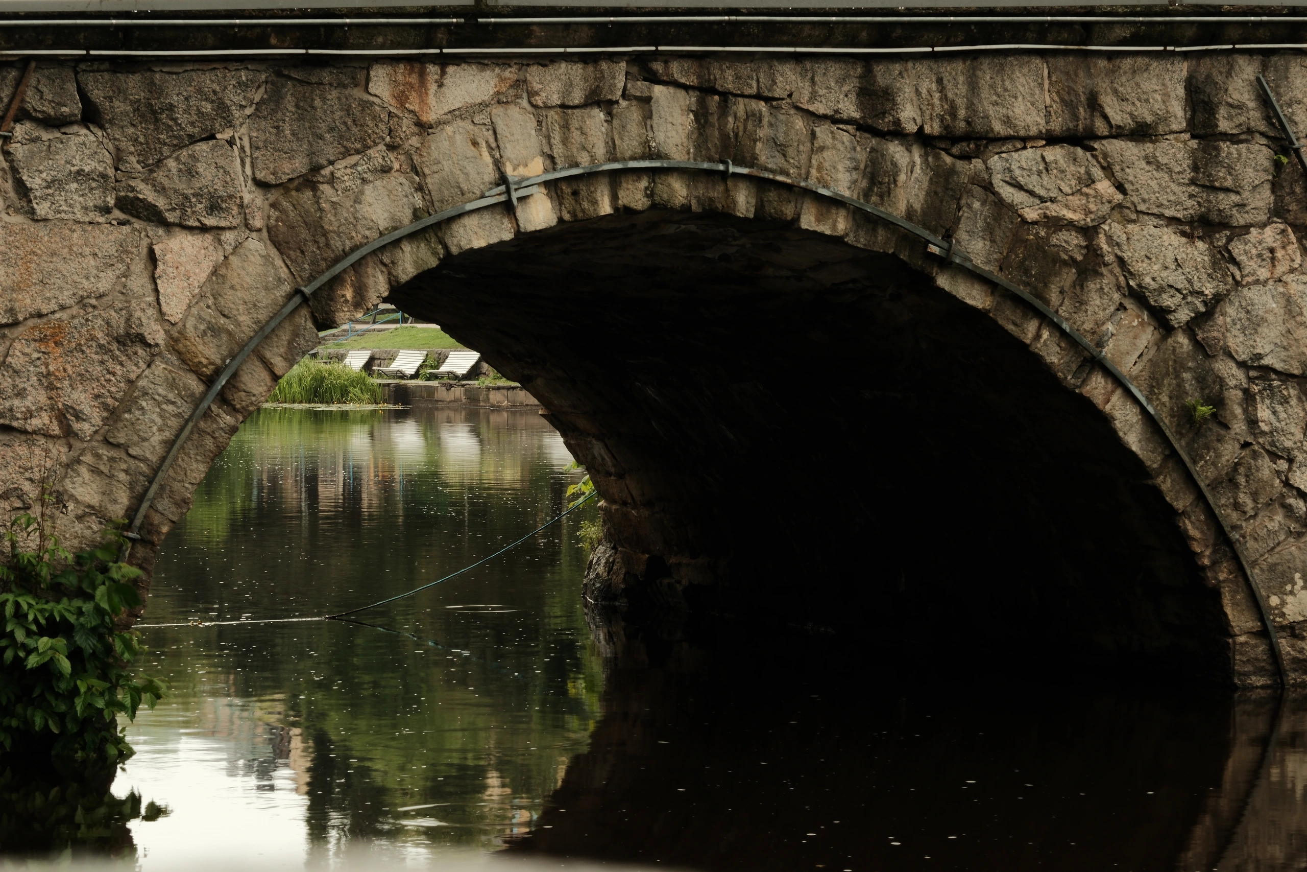 Stone bridge arch framing still water and green reflections