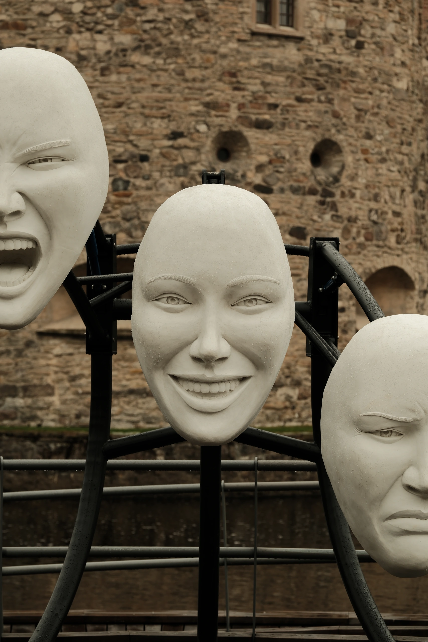 Three mannequin faces mounted against an old brick wall