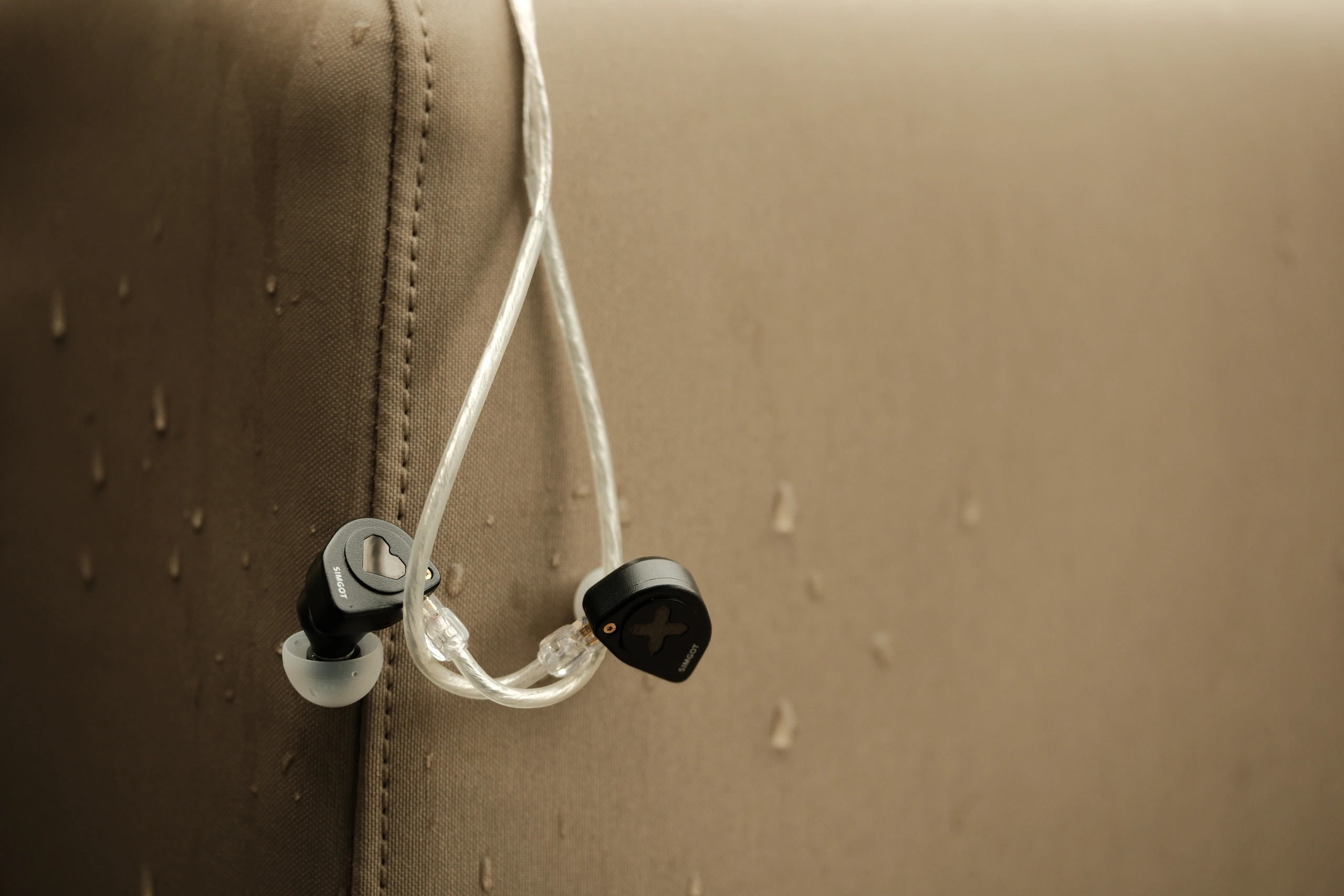 Wired earphones hanging against a rain-spotted surface