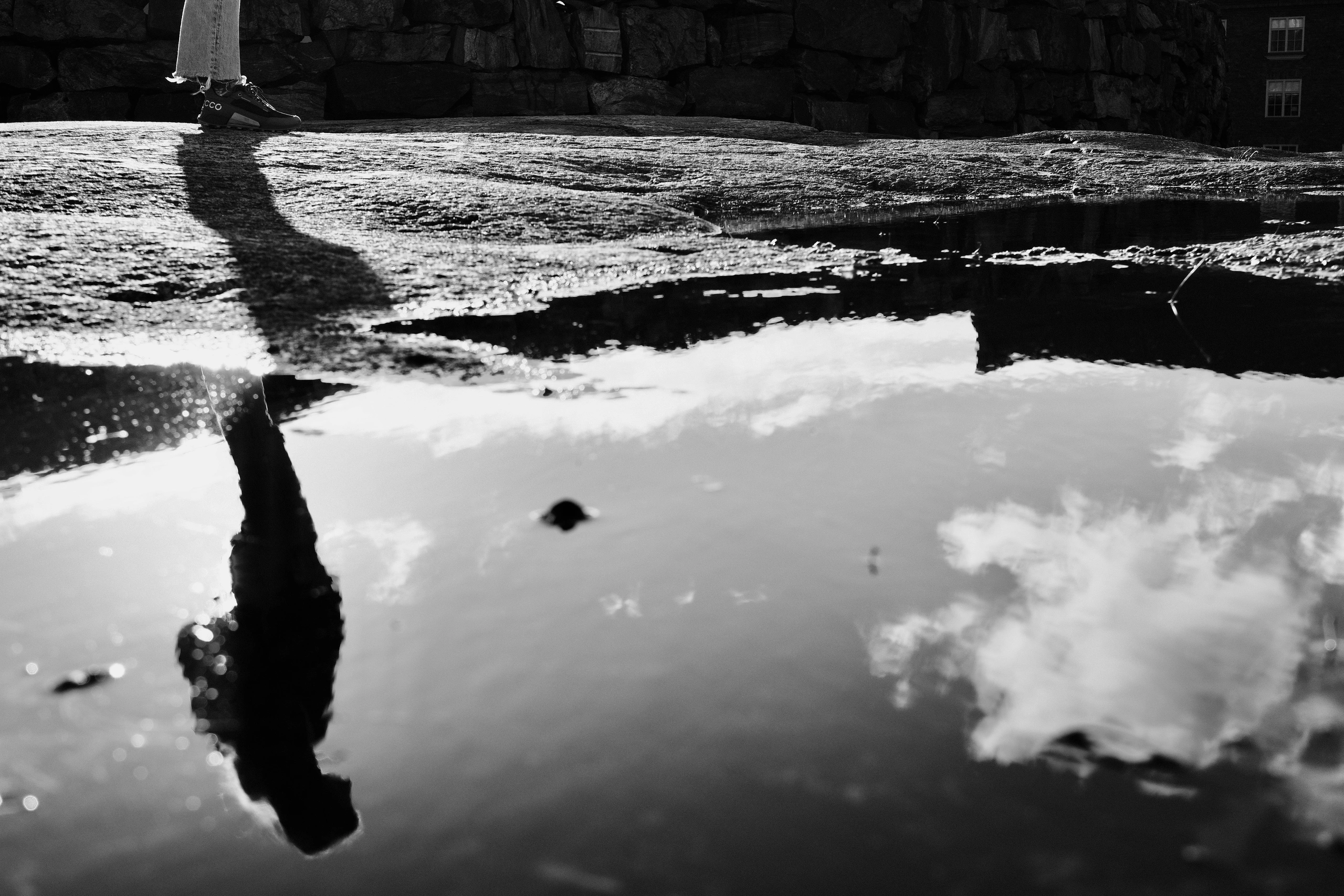 Pedestrian and cloudy sky reflected in a puddle
