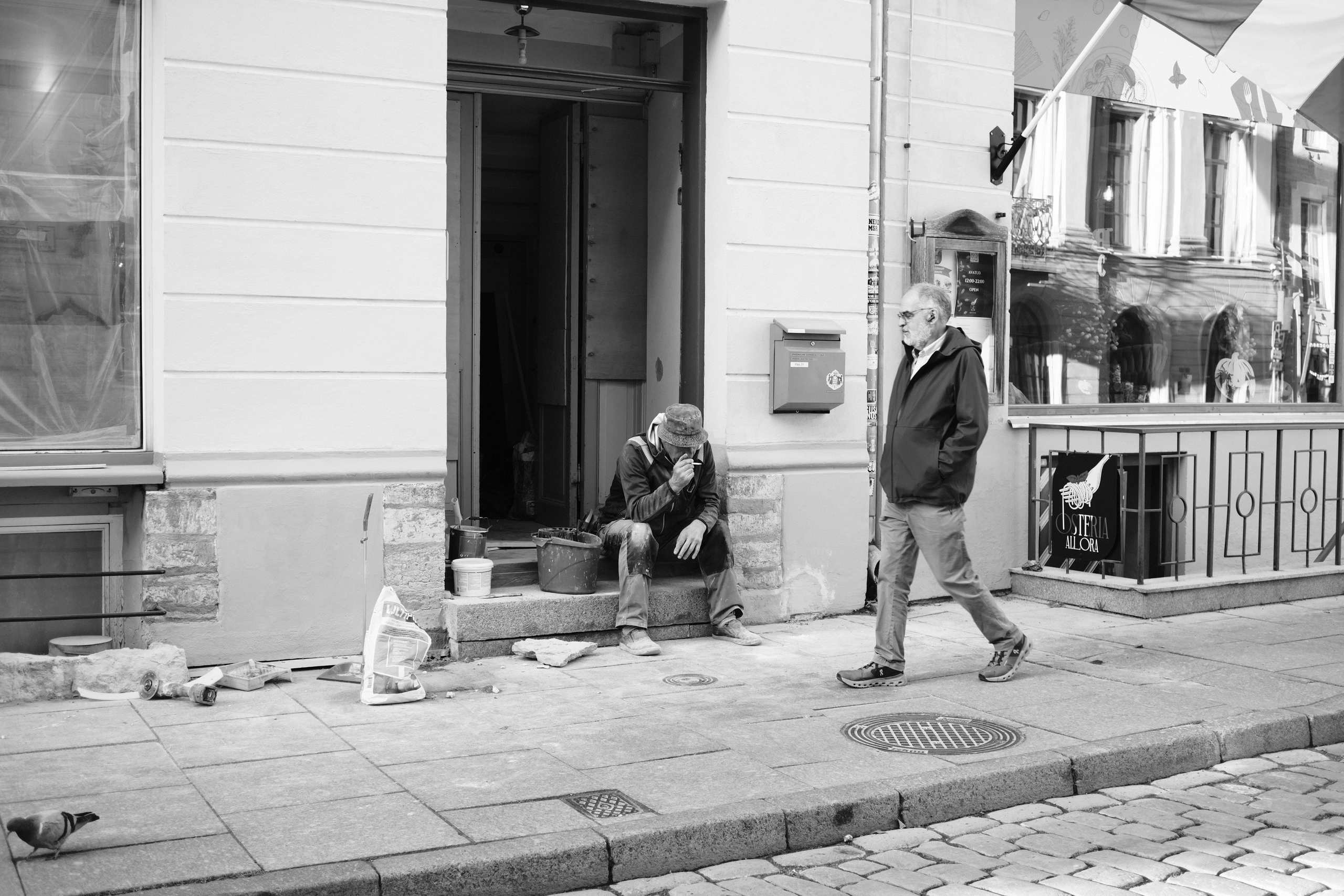 Pedestrian walking past a person seated outside a doorway